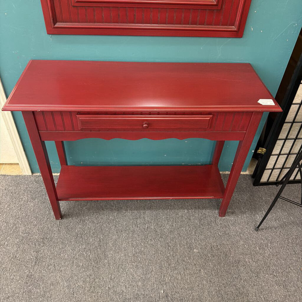 Red side table with a single drawer against a teal wall.