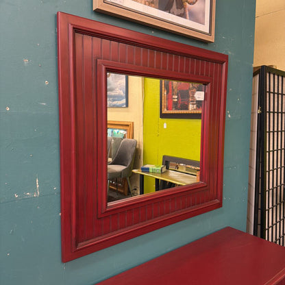 Red-framed mirror on a blue wall with reflections of a room.