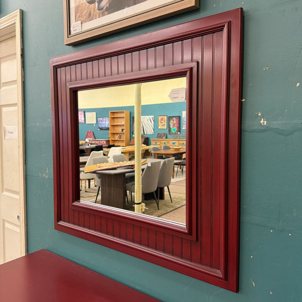 Red-framed mirror on a teal wall reflecting a room with tables and chairs.