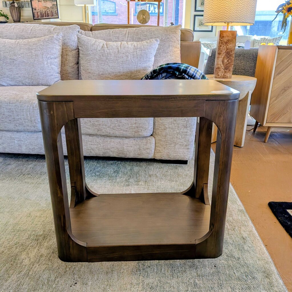 Wooden side table in a living room setting with a sofa and lamp in the background.
