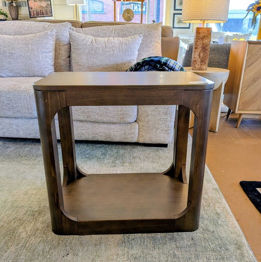 Wooden side table in a living room setting with a sofa and lamp in the background.