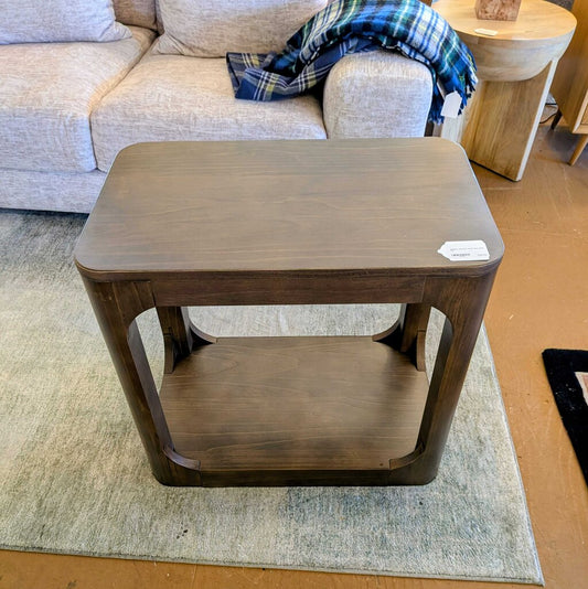 Wooden side table in a living room setting with a sofa and plaid blanket.