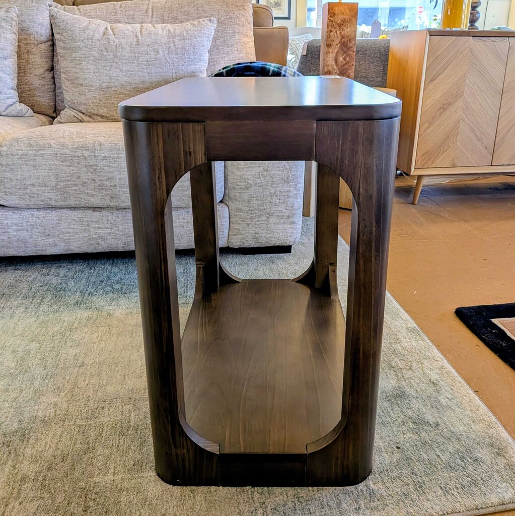 Wooden side table in a living room setting with a sofa and rug.