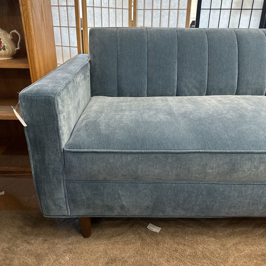 Blue velvet sofa in a room with wooden shelves and a window.