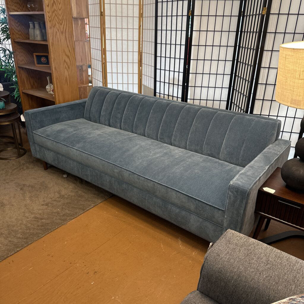 Gray sofa in a living room setting with a bookshelf and lamp.