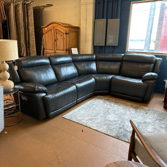 Black leather sectional sofa in a room with wooden flooring and a window.