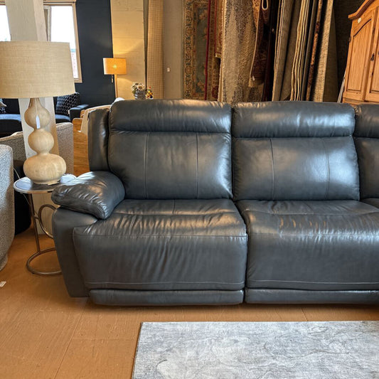 Gray leather sofa in a living room setting with lamps and curtains.