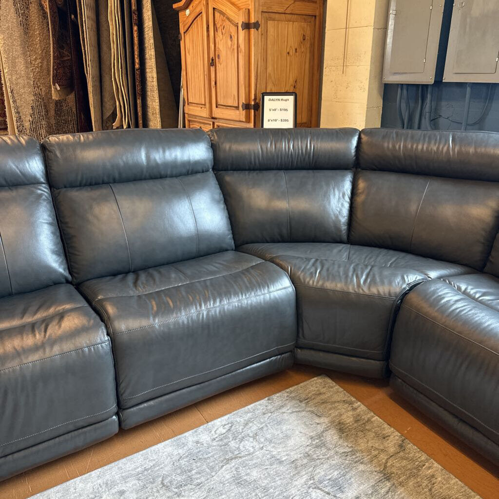 Gray leather sectional sofa in a room with wooden flooring and a door.