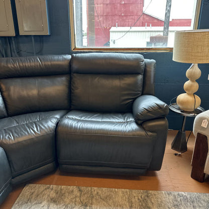 Black leather sectional sofa in a room with a window and lamp.