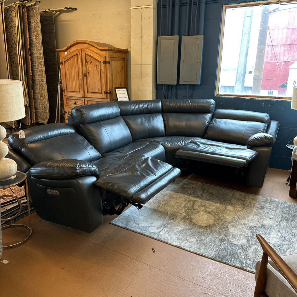 Black leather sectional sofa in a room with wooden furniture and a window.