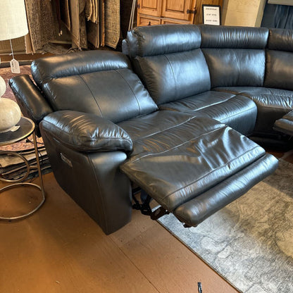 Black leather sectional sofa in a room with wooden flooring and a lamp.