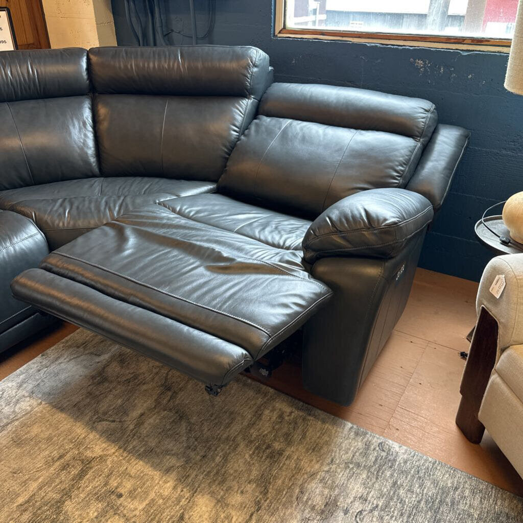 Black leather sectional sofa in a room with a blue wall and wooden floor.