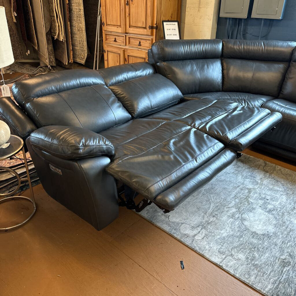Black leather sectional sofa in a room with wooden flooring and furniture.