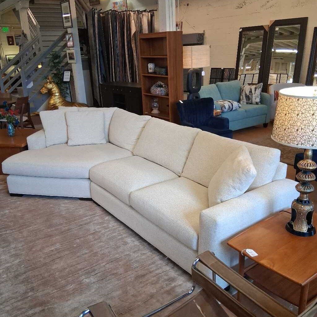 Beige sectional sofa in a furniture store with mirrors and a lamp in the background.
