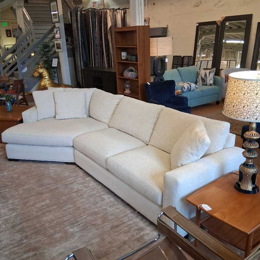 Beige sectional sofa in a furniture store with mirrors and a lamp in the background.