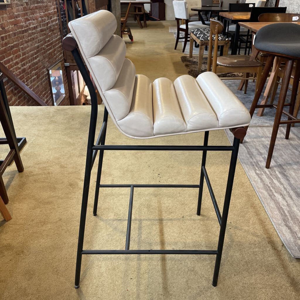 Beige cushioned bar stool with black metal frame in a casual dining setting.