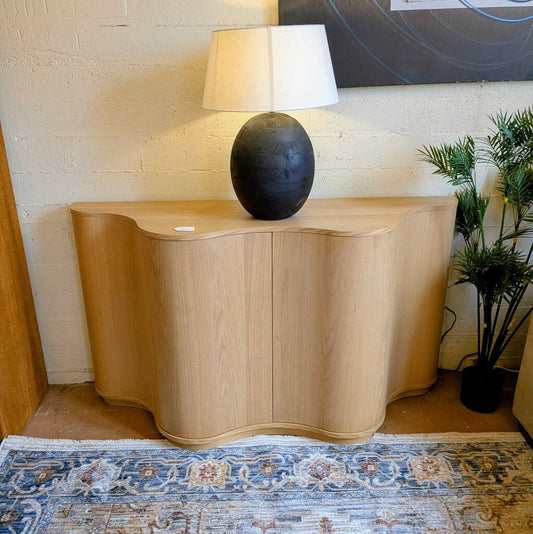 Wooden sideboard with a black lamp on top against a brick wall.