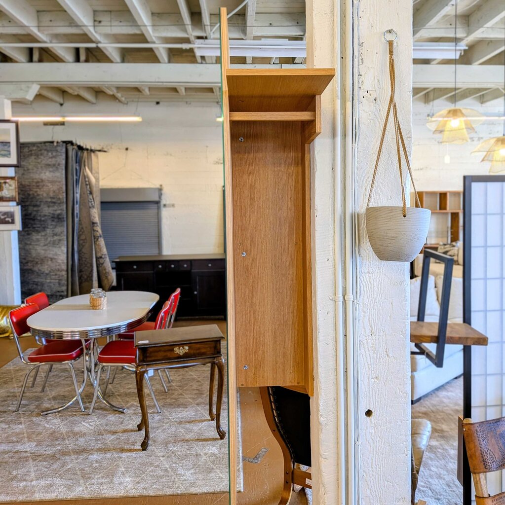 Wooden cabinet against a wall with a view of a kitchen and dining area in the background.