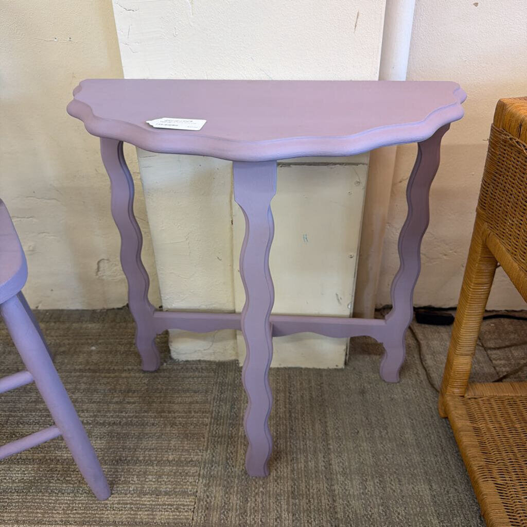 Small purple table with wavy legs against a neutral wall.