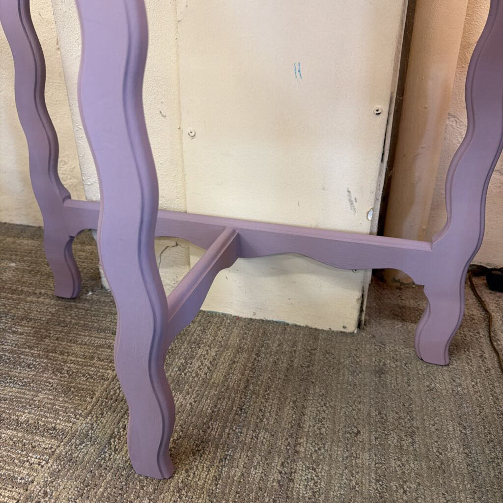 Purple side table with wavy legs on a carpeted floor.