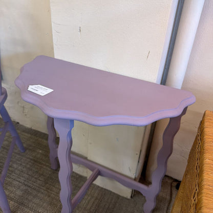 Purple side table with a scalloped edge against a neutral wall.