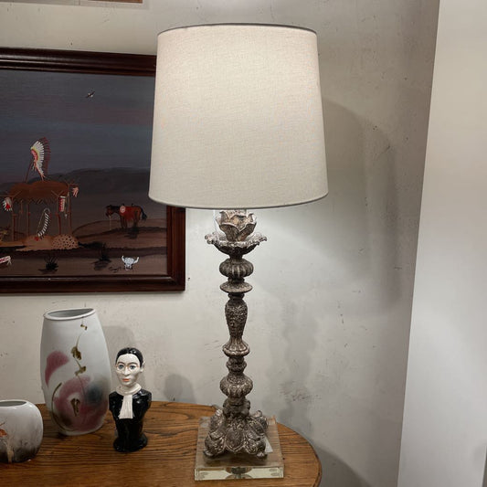 Decorative lamp on a table with a framed picture and small figurines in the background.