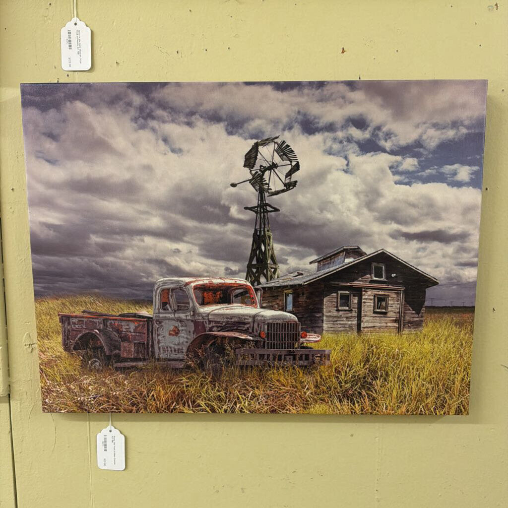 Vintage truck and windmill in a field with a wooden cabin under a cloudy sky, displayed on a wall.