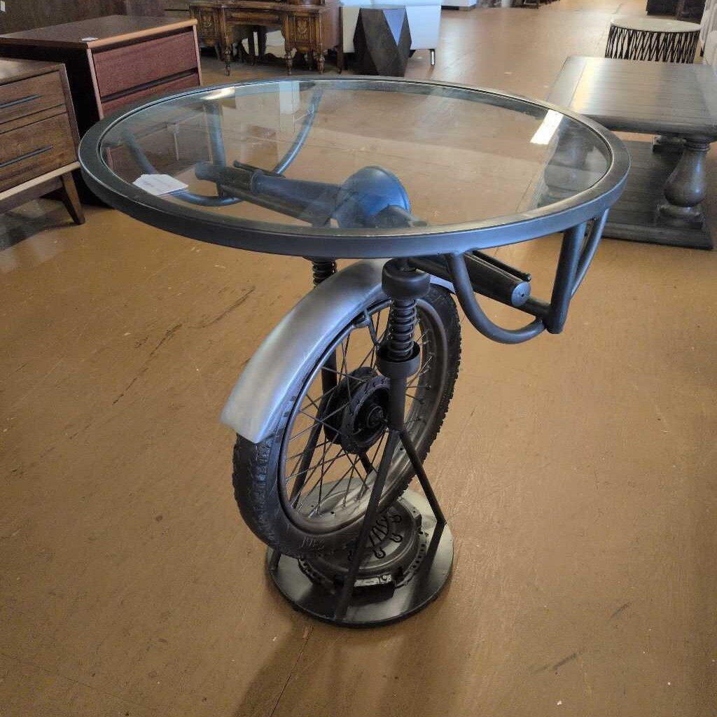 Table made from a repurposed bicycle frame with a glass top in an indoor setting.