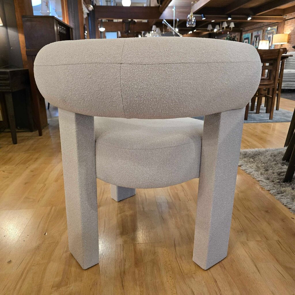 Beige upholstered stool on a wooden floor with a blurred indoor background