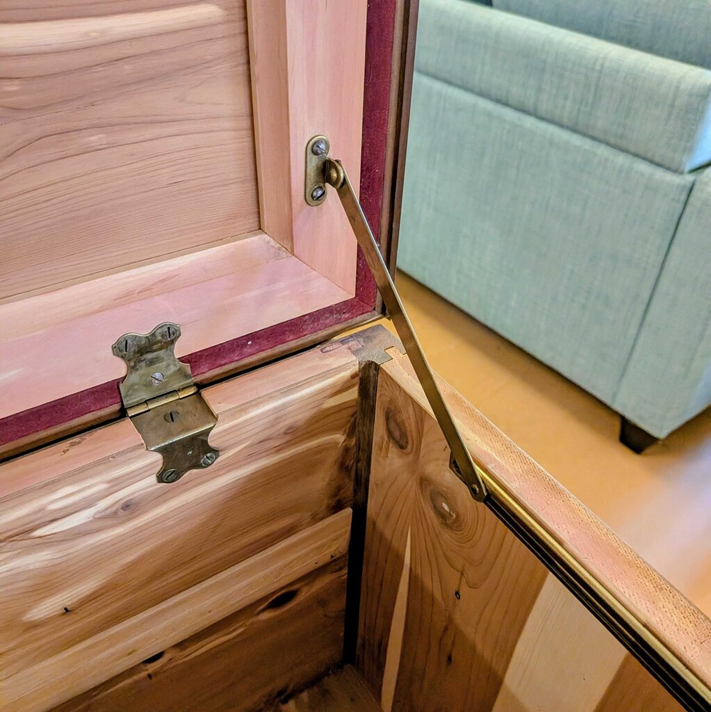 Wooden jewelry box with a hinged lid, partially open, on a wooden surface.