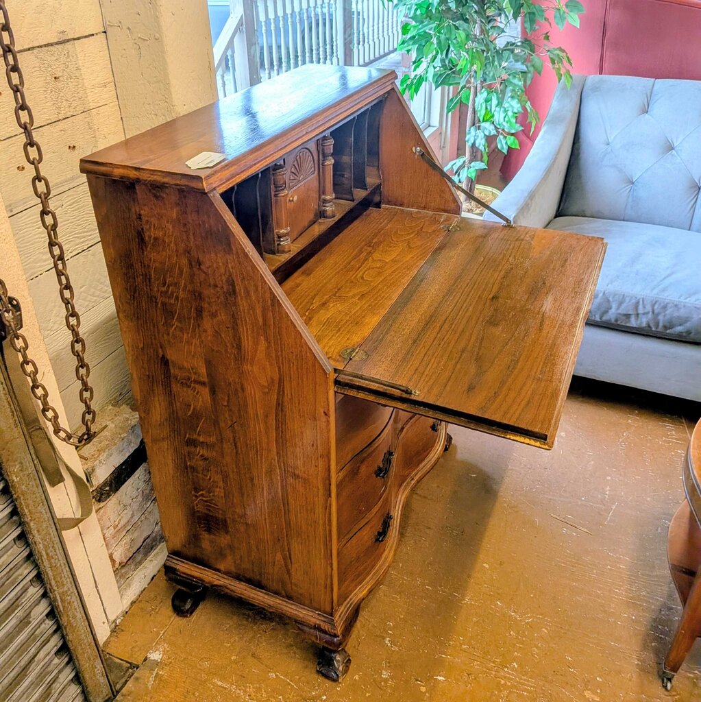 Wooden secretary desk with open flap in a room with a couch and plant