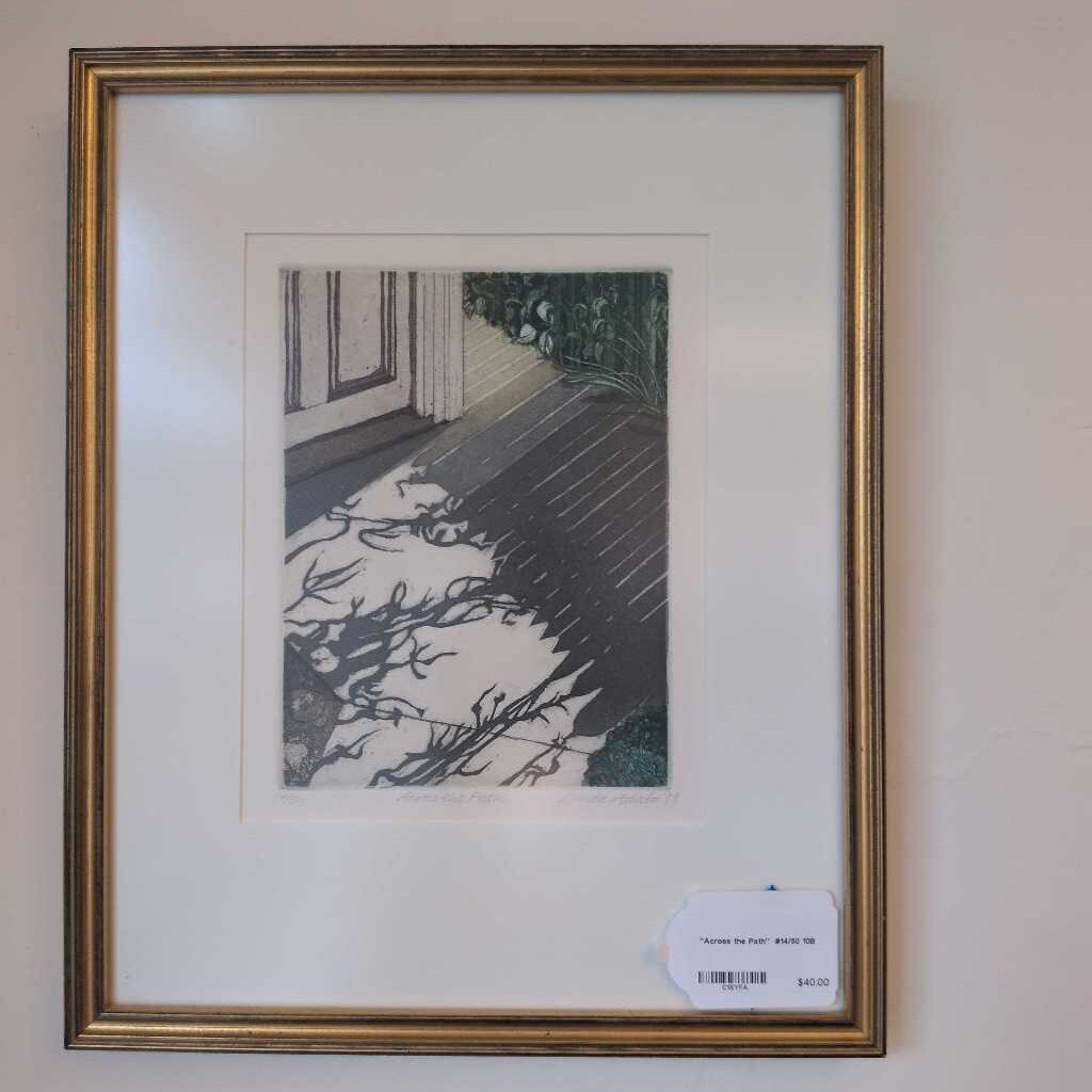 Framed artwork of a landscape with trees and a path on a beige wall.