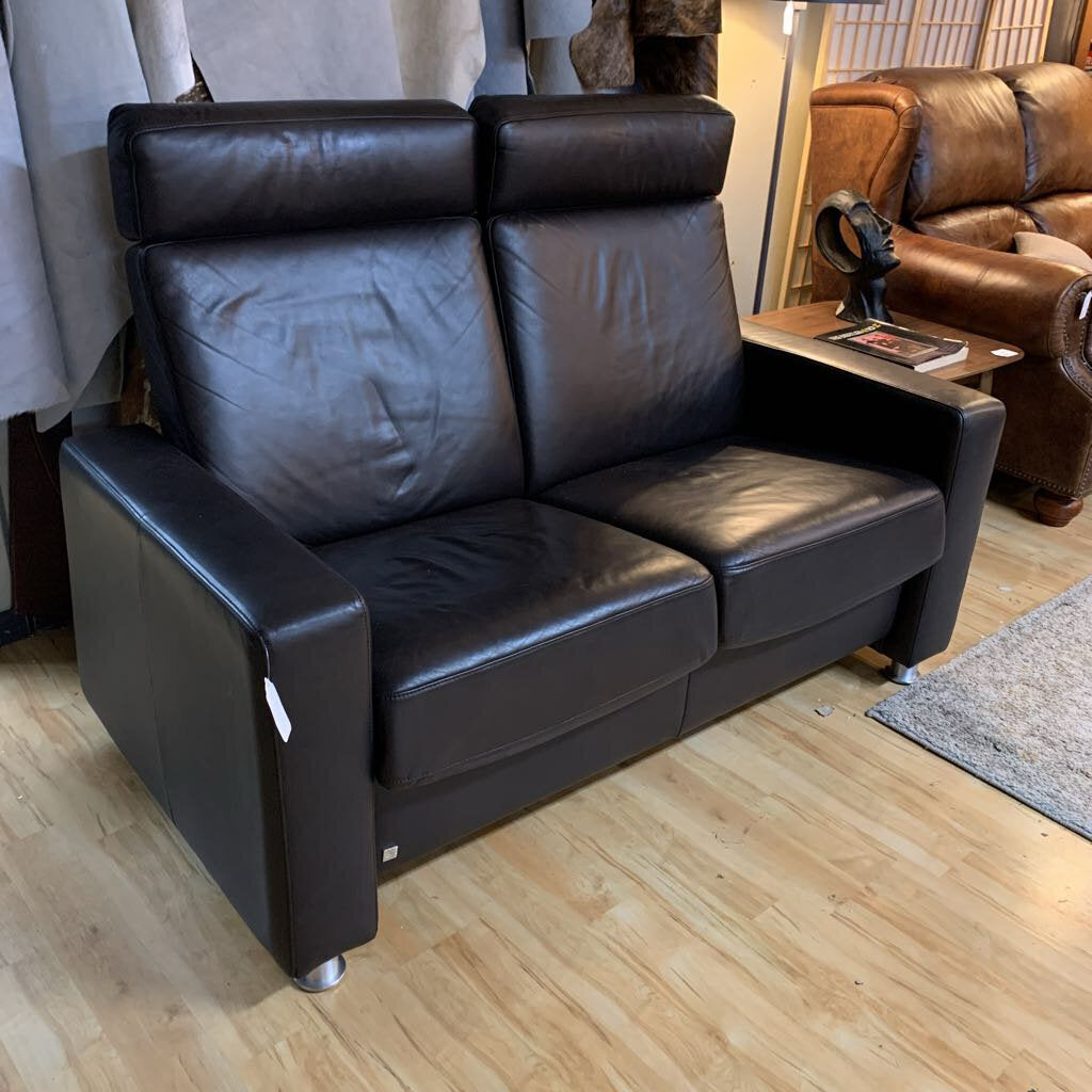Brown leather sofa in a showroom setting with other furniture in the background.