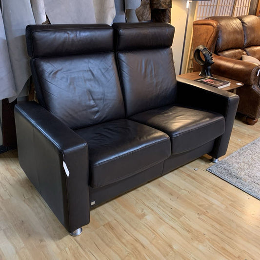 Brown leather sofa in a showroom setting with other furniture in the background.