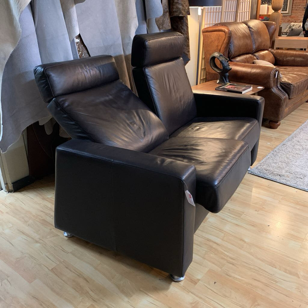 Black leather recliner chair in a room with wooden flooring and another brown leather couch.