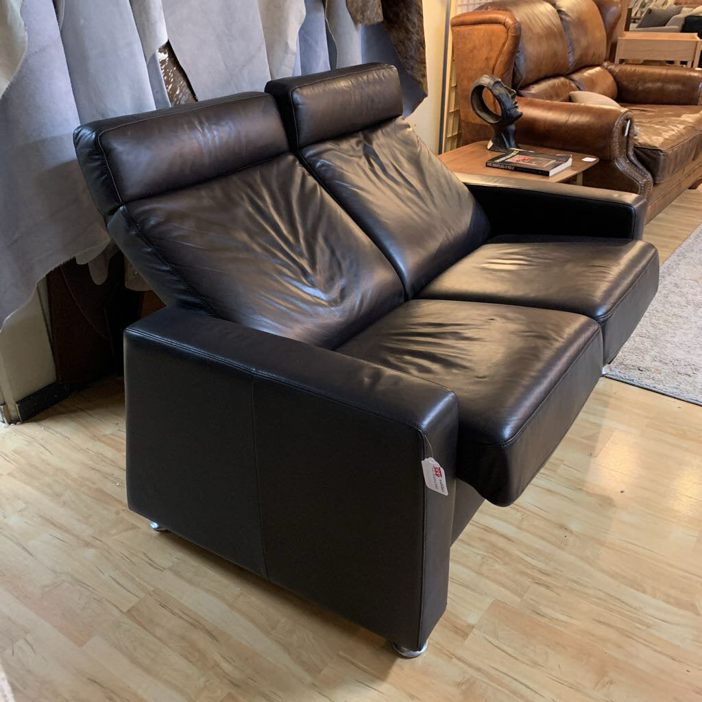 Black leather sofa in a room with wooden flooring and other furniture.