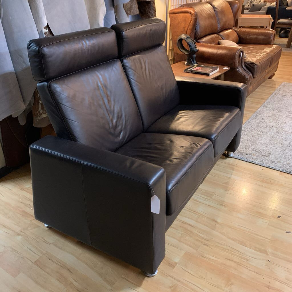 Black leather sofa in a showroom setting with wooden flooring.
