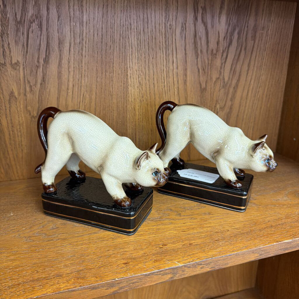 Two white cat figurines on black bases against a wooden background