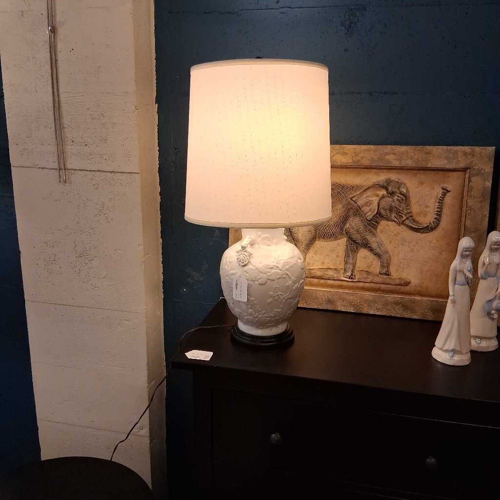 Lamp on a dark surface with decorative items including an elephant painting and statues.