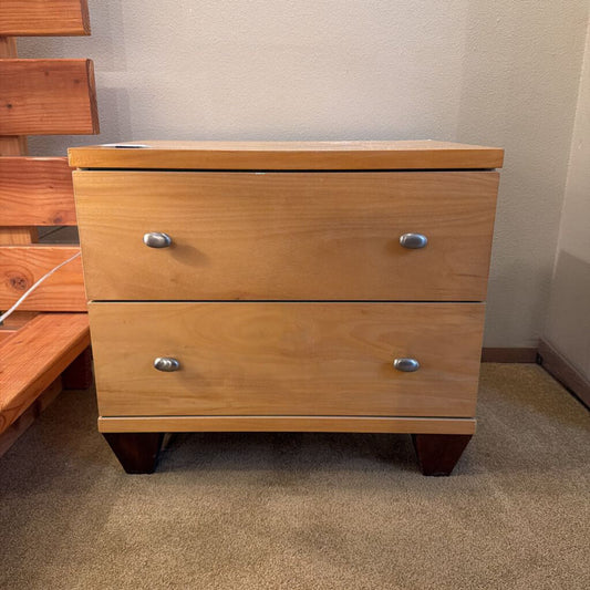 Wooden nightstand with two drawers on a carpeted floor.