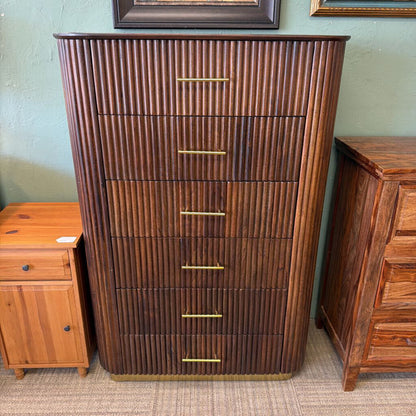 Wooden dresser with vertical slats and gold handles against a green wall.