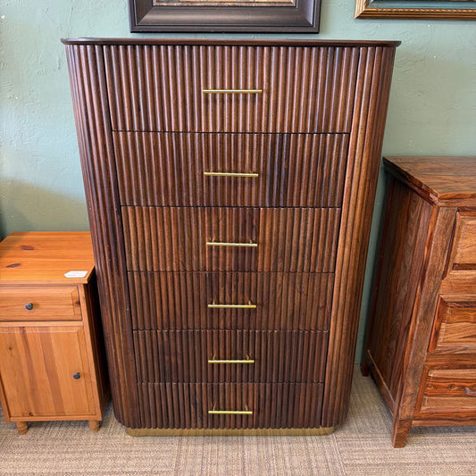 Wooden dresser with vertical slats and gold handles in a room setting.