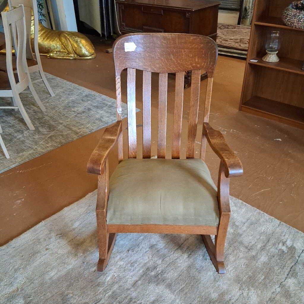 Wooden chair with a green cushion on a patterned rug in a room with furniture.