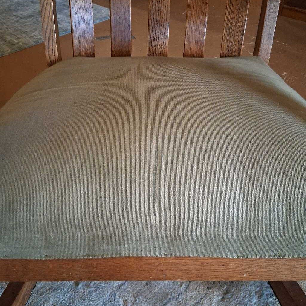 Wooden chair with a green cushion on a wooden floor.