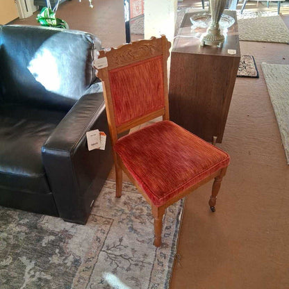 Wooden chair with red cushion on a carpeted floor next to a black sofa.