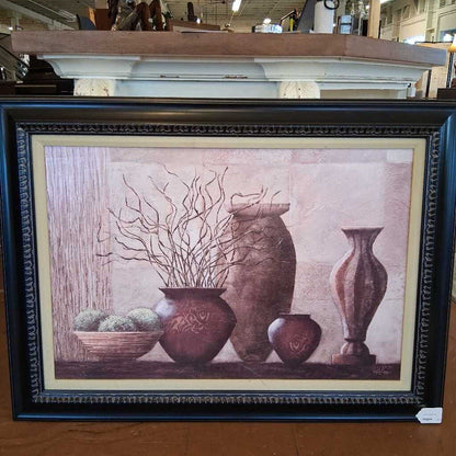 Framed artwork with decorative vases and branches on a wooden surface