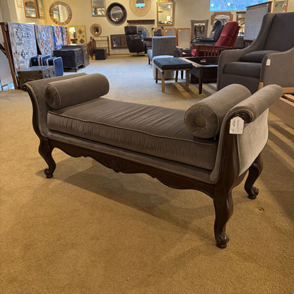 Gray upholstered bench with wooden legs in a furniture store setting