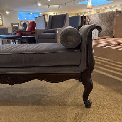 Gray upholstered bench with dark wood legs in a showroom setting