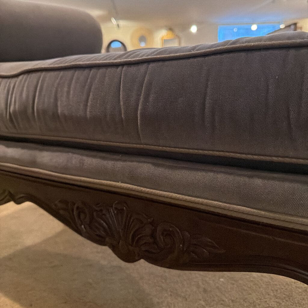 Close-up of a gray upholstered chair with ornate wooden legs.