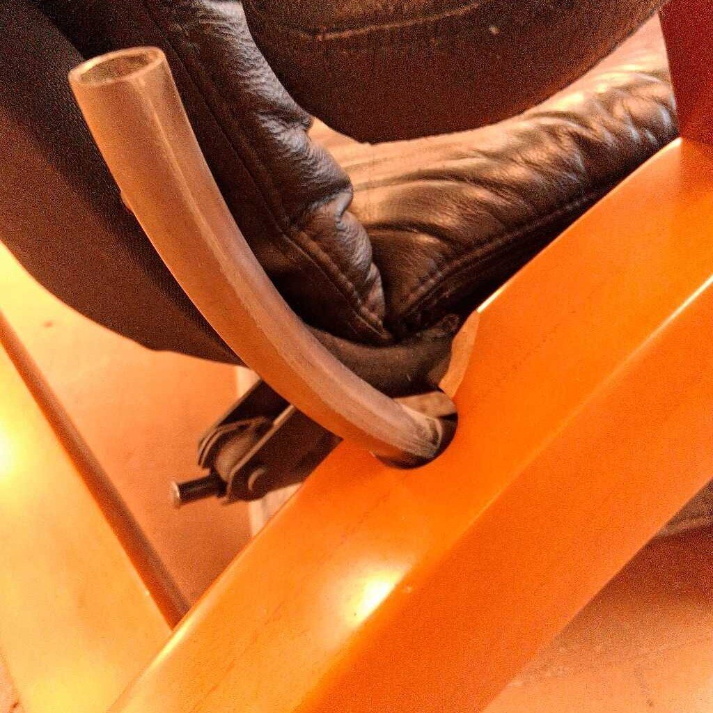 Close-up of a person wearing brown leather boots with a metal buckle on an orange chair.
